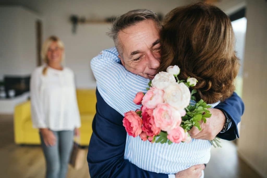 The man is hugging the woman while holding a bouquet of flowers.
