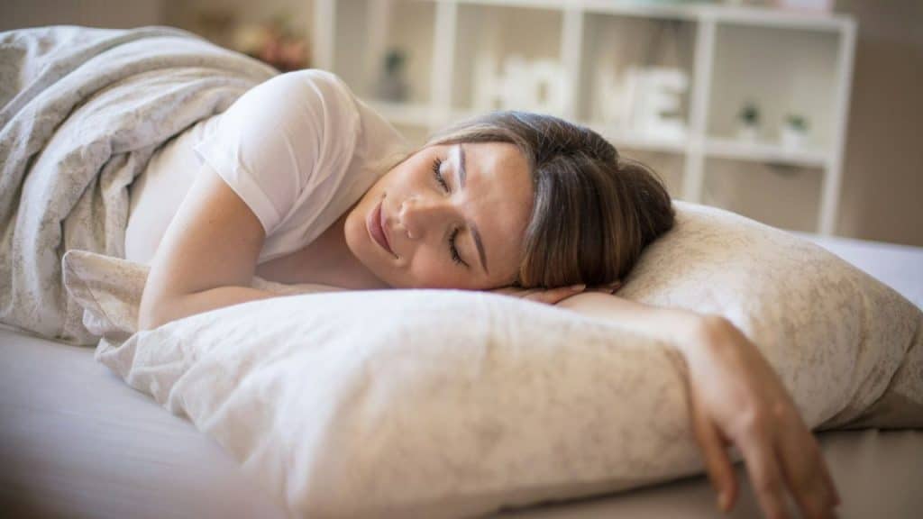 A woman in a white shirt is sleeping peacefully on a large pillow in bed.