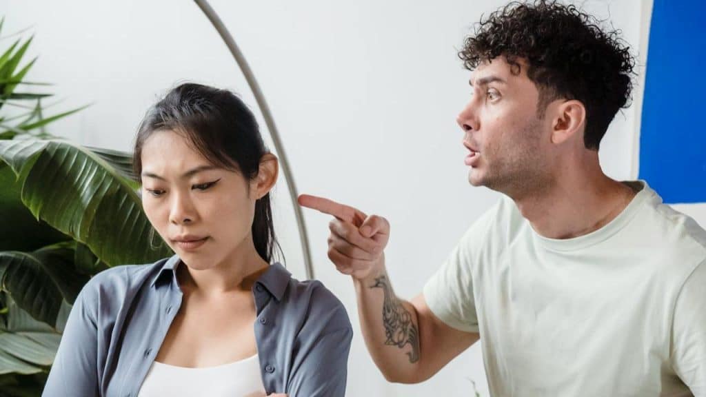 A man is pointing his finger at a woman who is looking down with a sad expression.