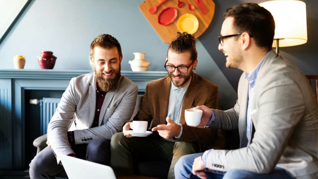 Three stylish, smiling men are having a casual business meeting over coffee.