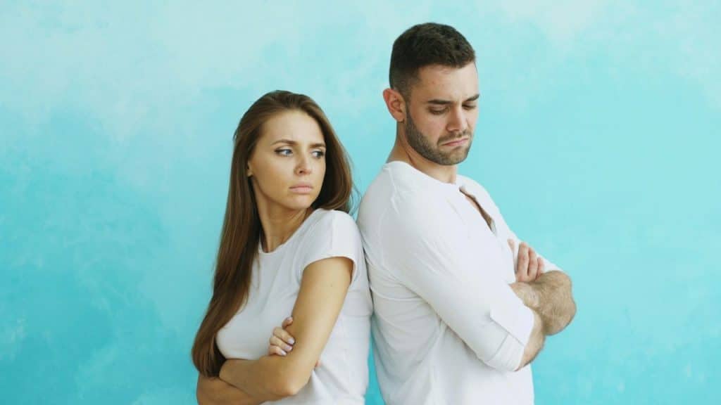 Man and woman in white shirts standing back-to-back with arms crossed.
