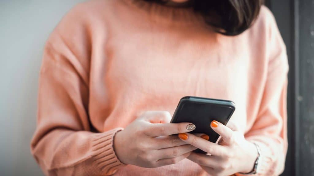 A woman wearing a pink sweater holding a smartphone and typing.