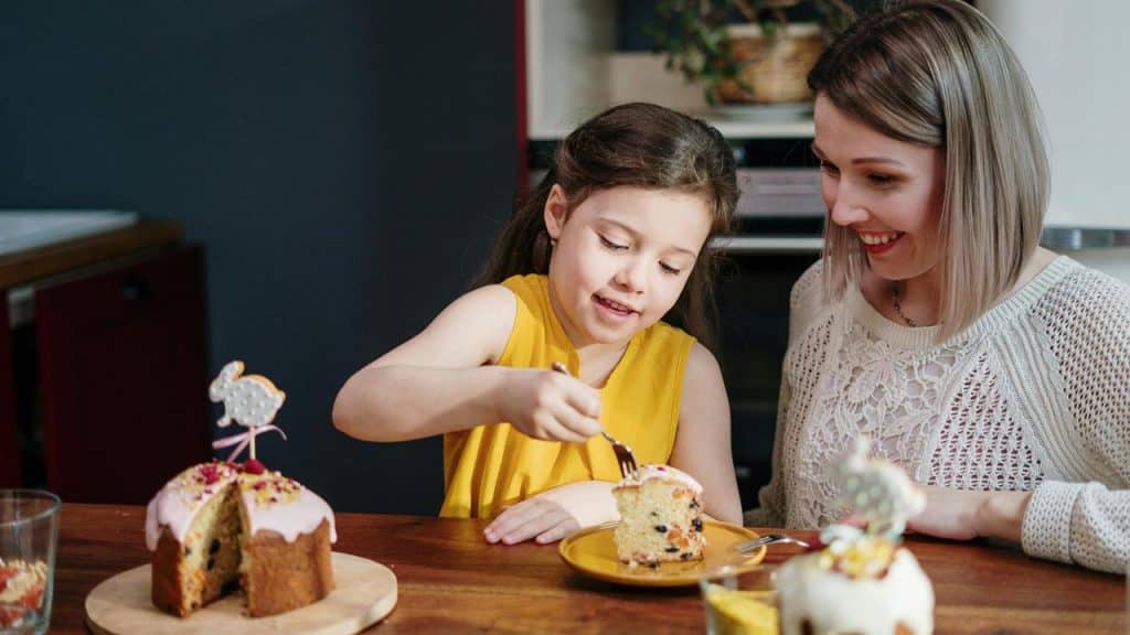 A mother and daughter sitting at a table enjoying cake together.