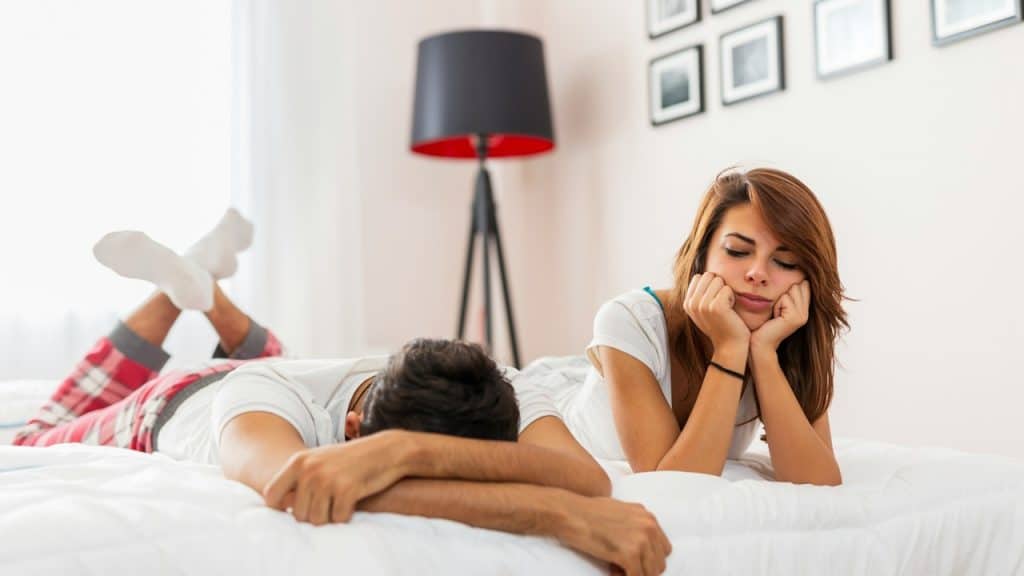 A woman holding her head in her hands and looking at her partner who has his face hidden in his arms. 