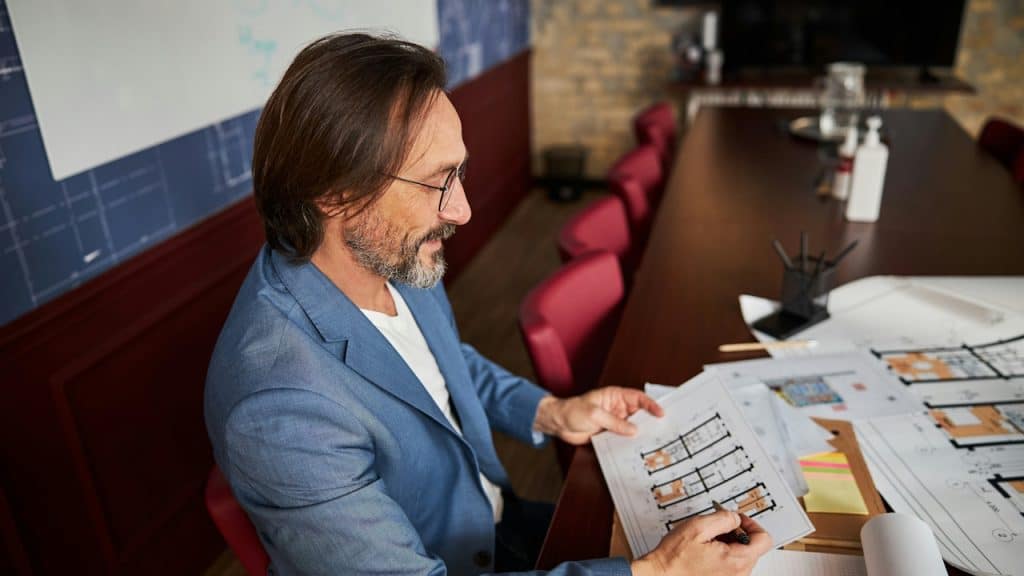 A bespectacled man looking at documents while sitting at a table.