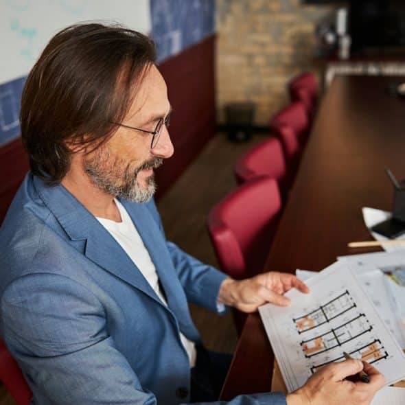 A bespectacled man looking at documents while sitting at a table.
