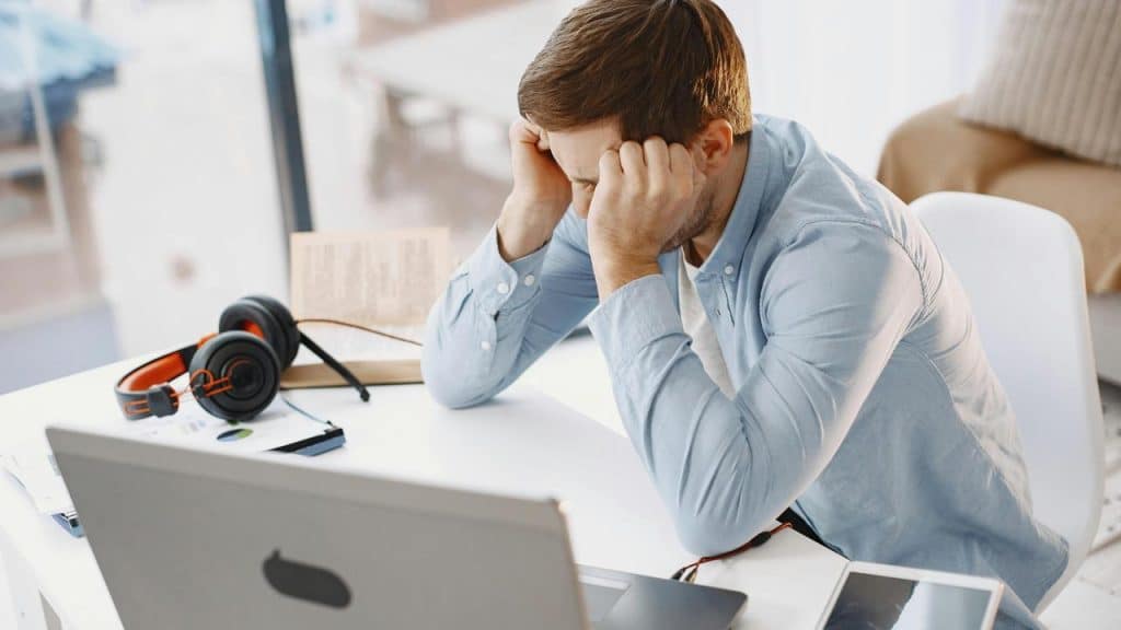 A man sitting at a desk with his head in his hands in front of a laptop.