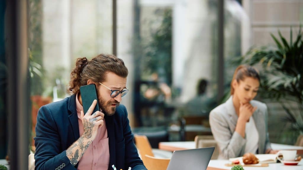 Busy entrepreneurs using laptops while communicating over mobile phones in a cafe.