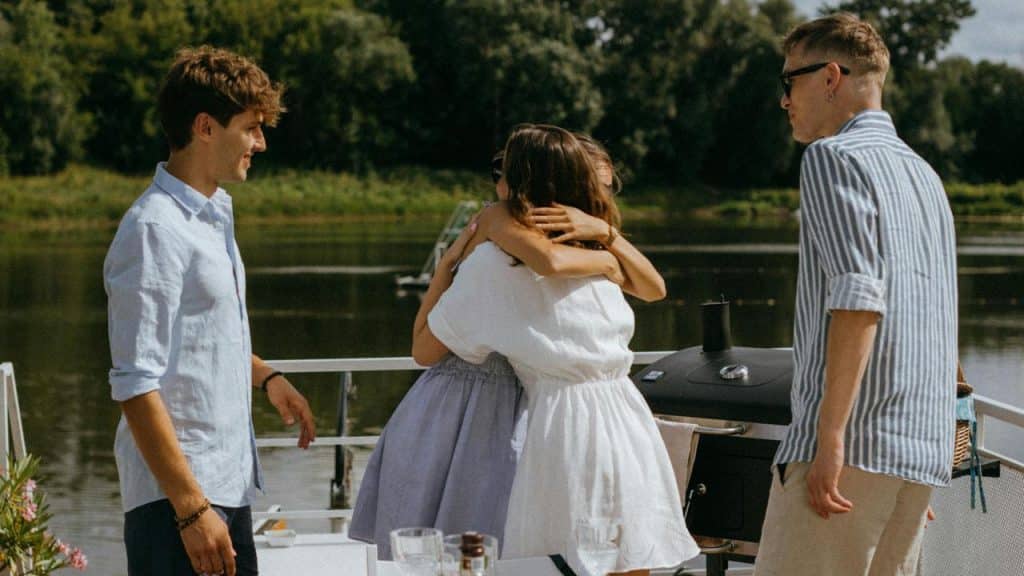 A group of friends greeting each other with a hug near a lake.