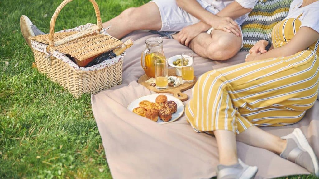 A couple enjoying a picnic on a blanket with snacks and drinks in the grass.
