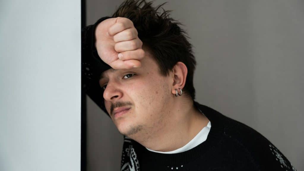 Young man with earrings and a mustache resting his fist on his forehead.