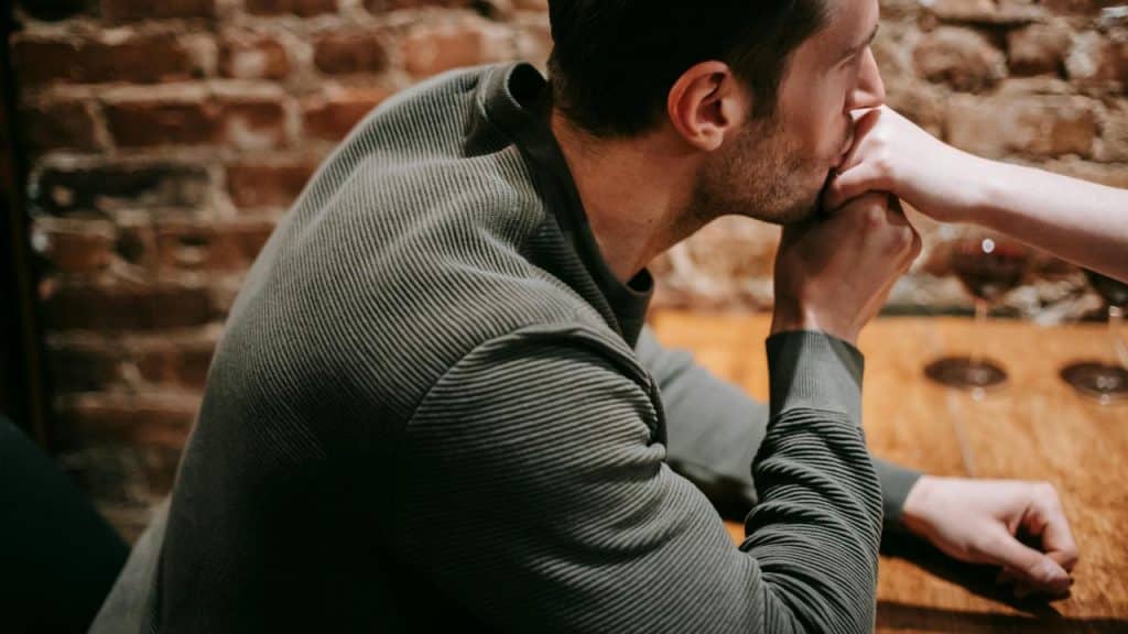 A man kissing a woman's hand while sitting at a wooden table.