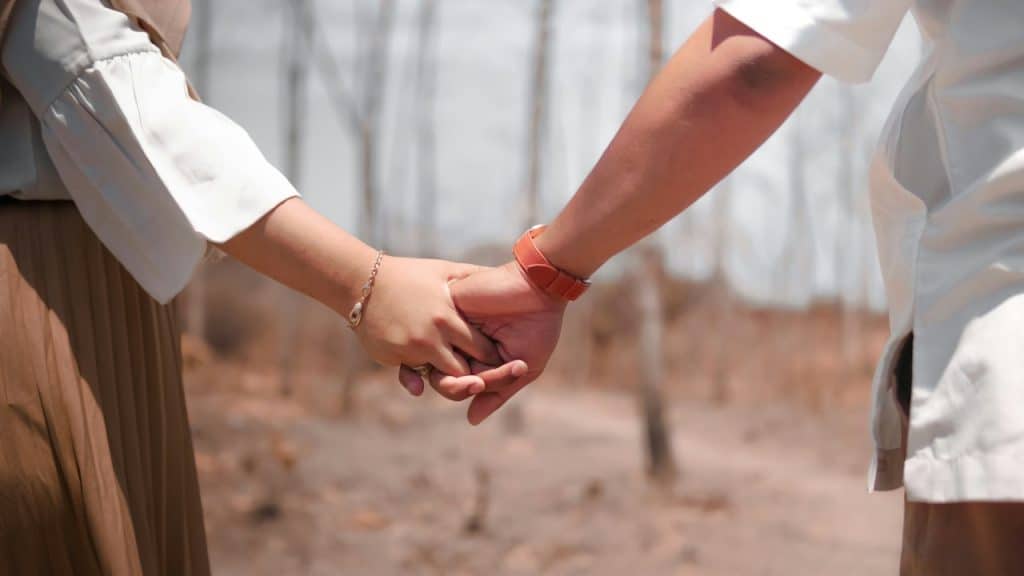 A close-up of a couple holding hands while standing in a dry, outdoor setting.