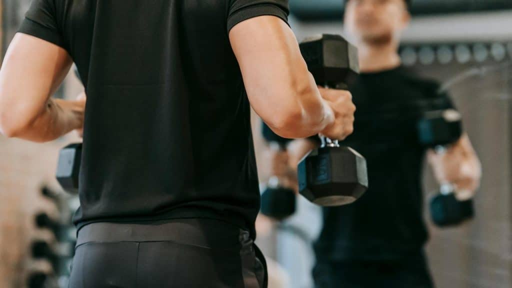 A man lifting dumbbells in front of a mirror at the gym.