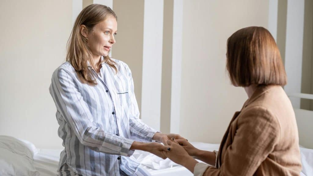 A woman in pajamas holding hands and talking with another woman.