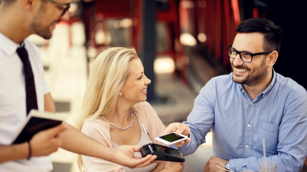 Happy couple making contactless payment with smartphone after lunch in a restaurant.