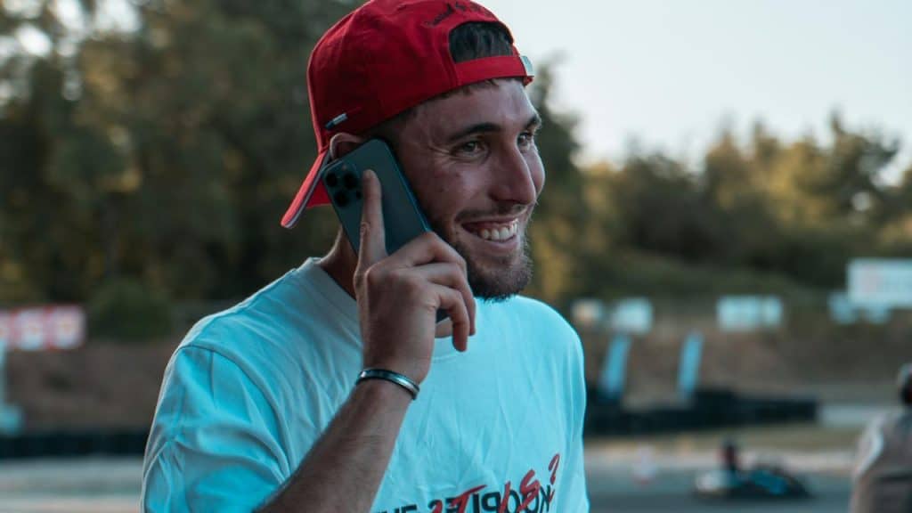 A smiling man in a red cap talking on a phone outdoors.
