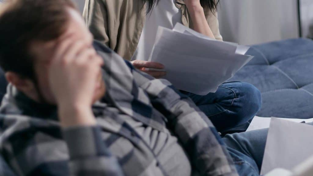A couple sitting with bills, both appearing stressed and overwhelmed.