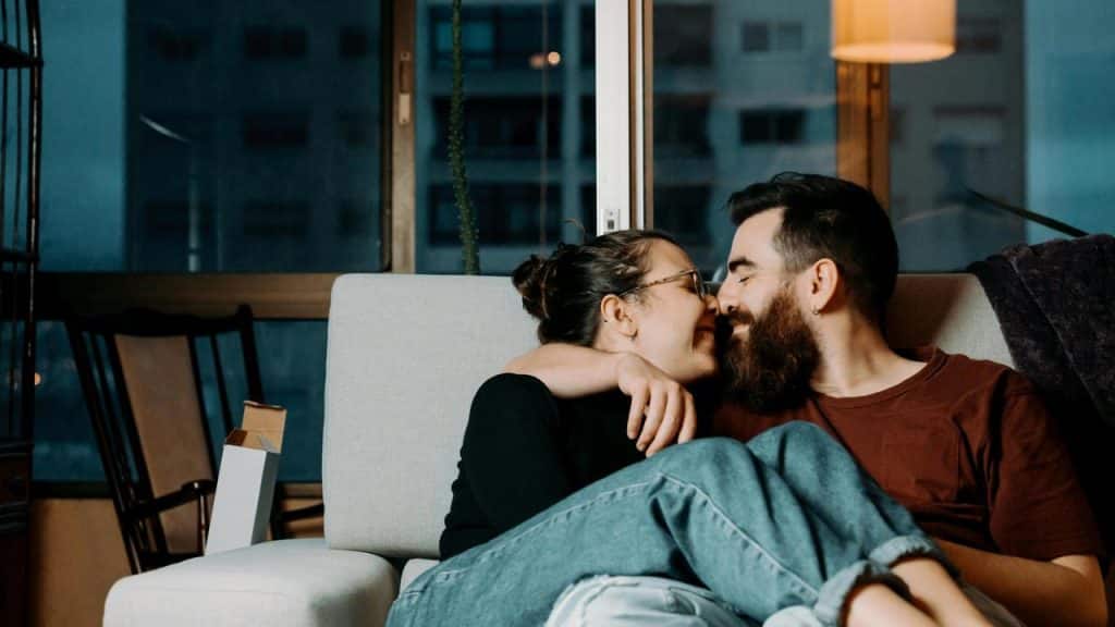 A couple sitting on a couch, smiling and leaning in close to each other.