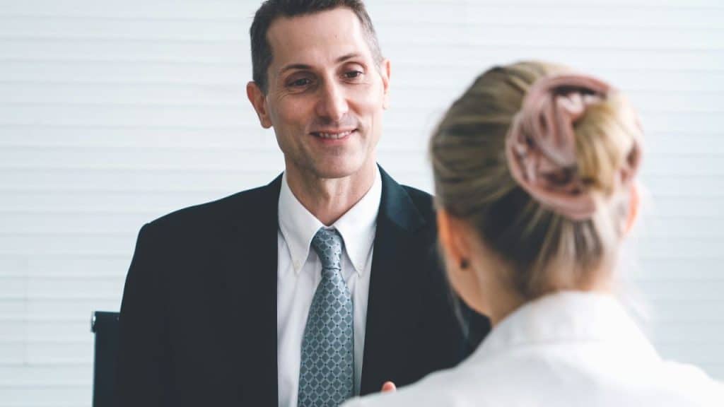 Smiling man in a suit and tie looks across a table at a woman with her back turned.