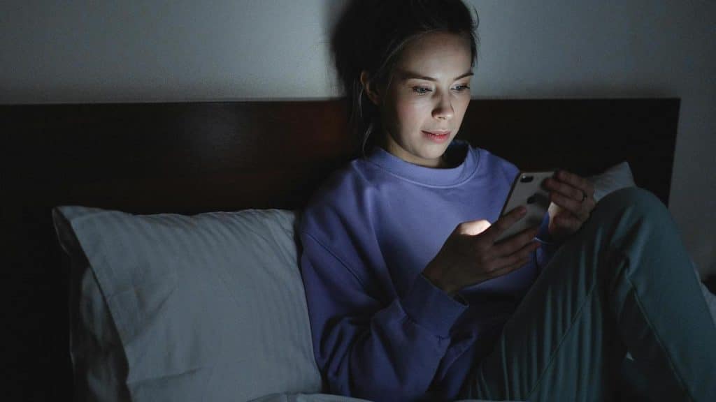 A woman sitting in bed at night looking at her phone.