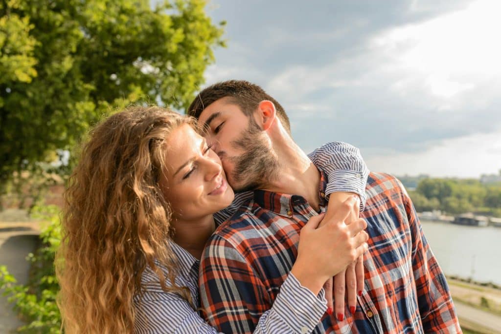 The woman smiles as the man kisses her.