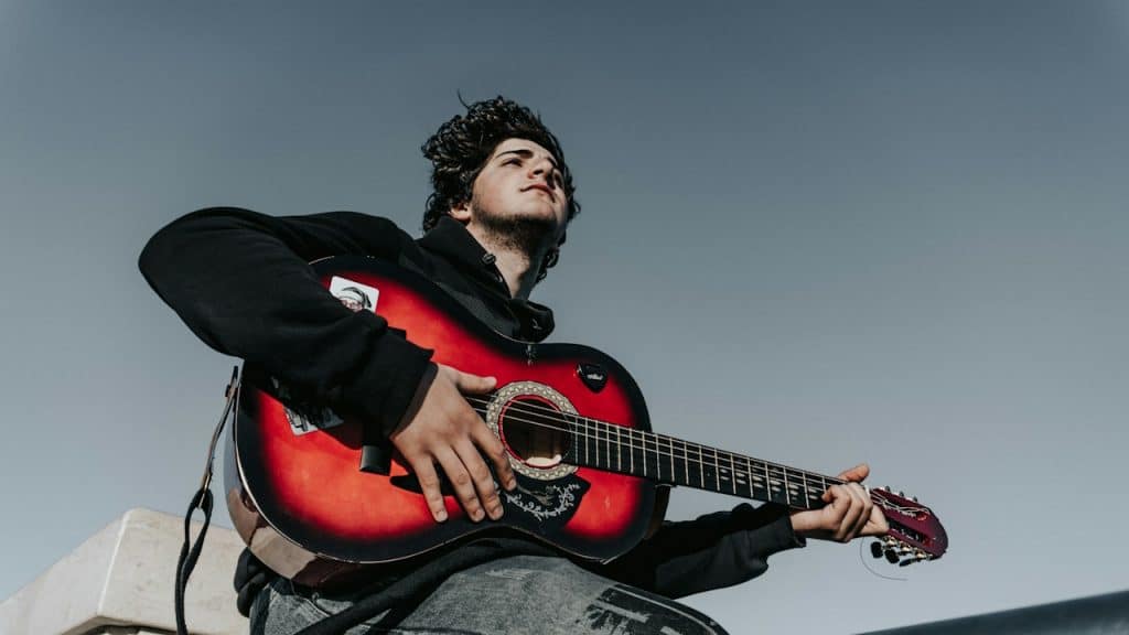 A man plays guitar with a blue sky background.