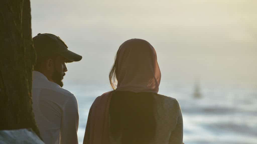 A couple looking toward a blurry ocean with moderate waves.