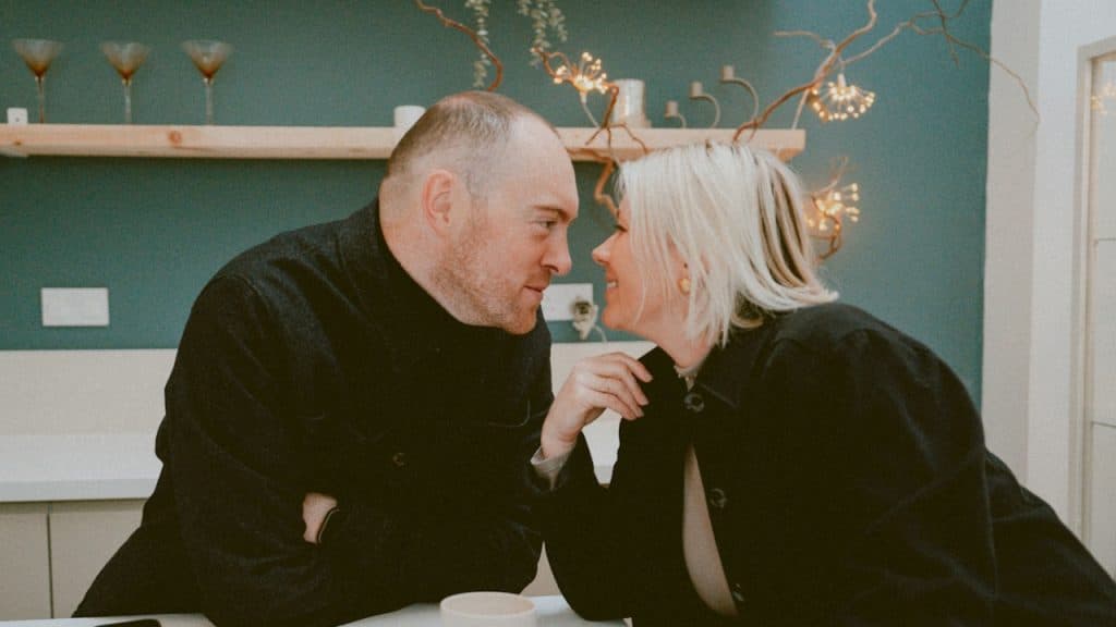 A middle-aged couple on a date sitting face-to-face, looking into each other's eyes, leaning in for a kiss.