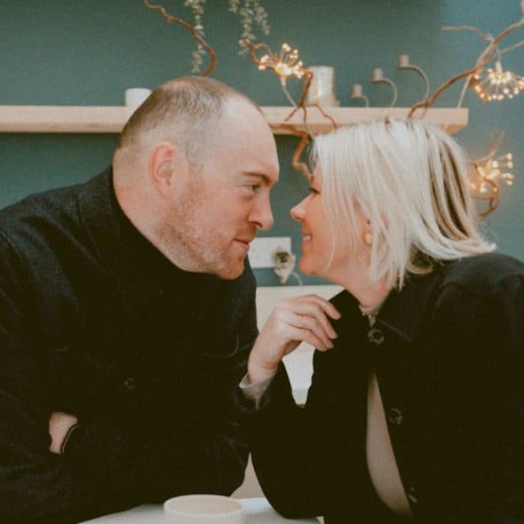 A middle-aged couple on a date sitting face-to-face, looking into each other's eyes, leaning in for a kiss.