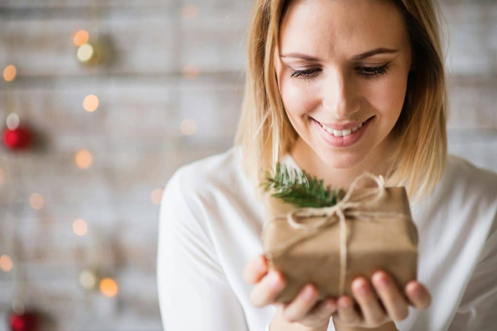 The woman is smiling while holding her Christmas present.