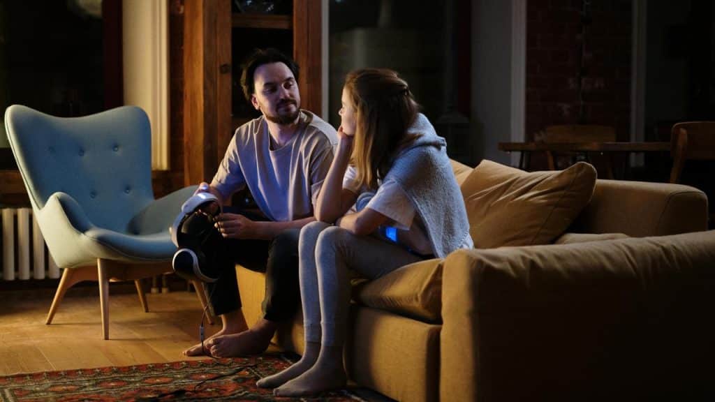 A couple sitting on a couch at home, talking in a cozy evening setting.