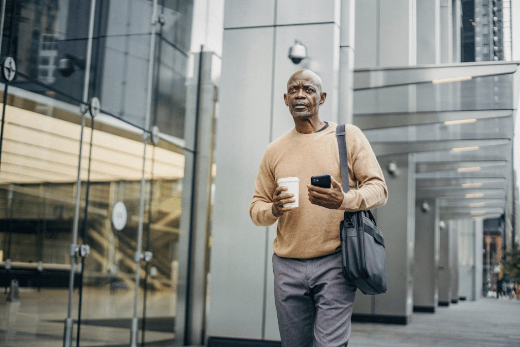 Serious man with takeaway coffee and smartphone on street