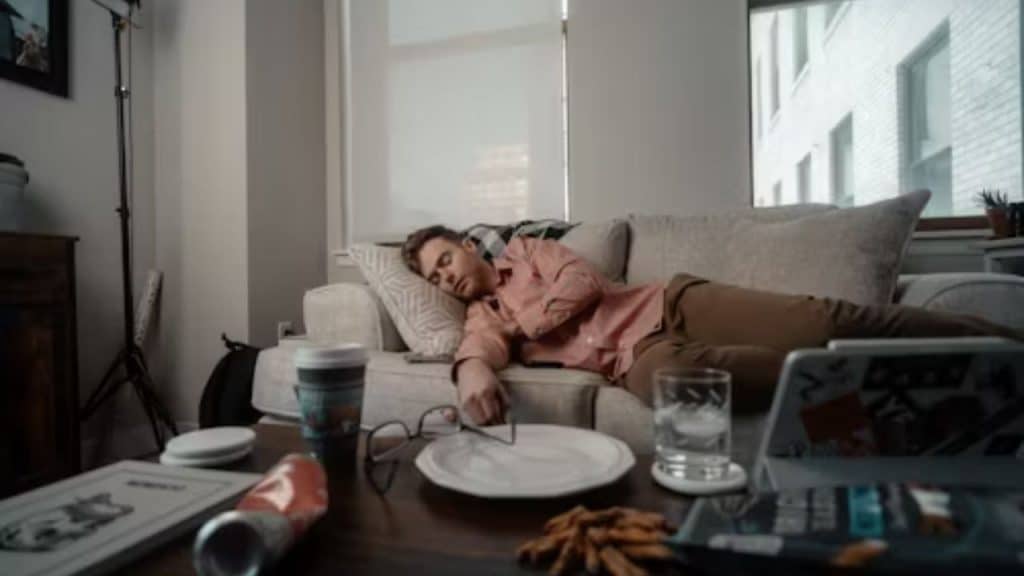 Man falling asleep on the couch with a plate and a glass on the table