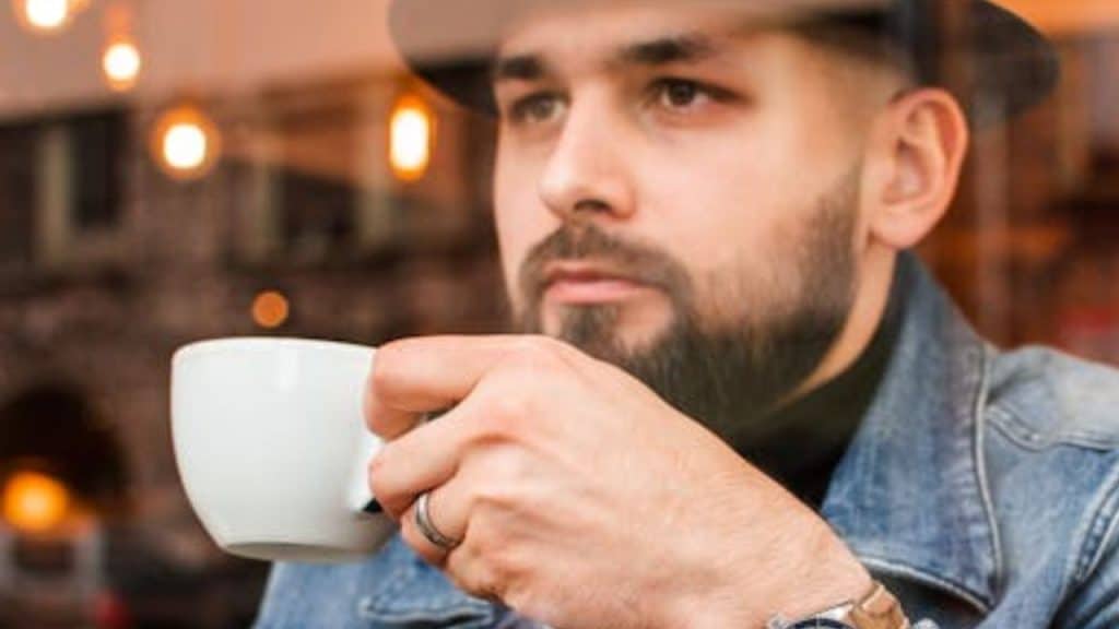 Man staring blankly out the window while drinking coffee