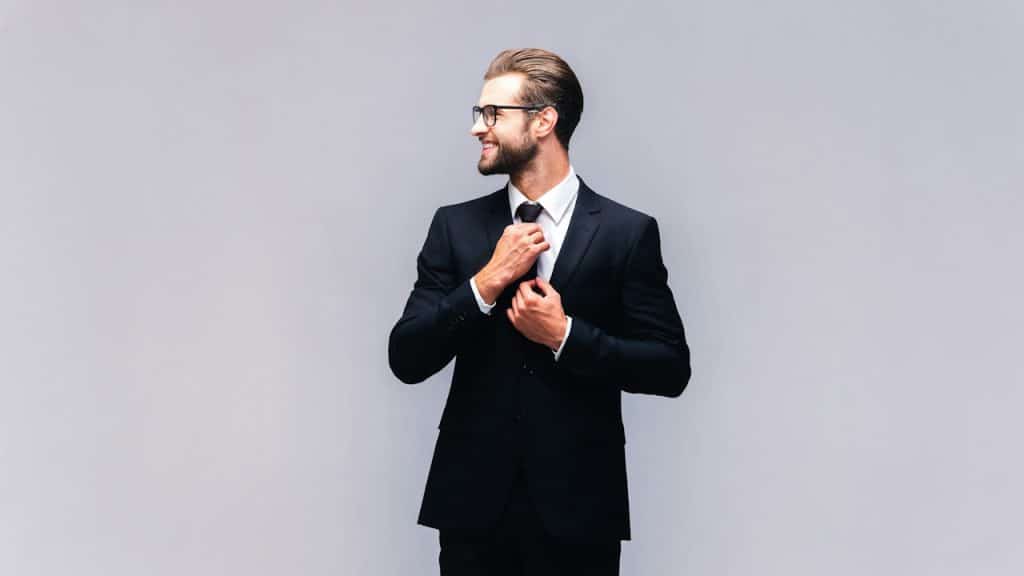 A man in a full suit adjusting his necktie and smiling.