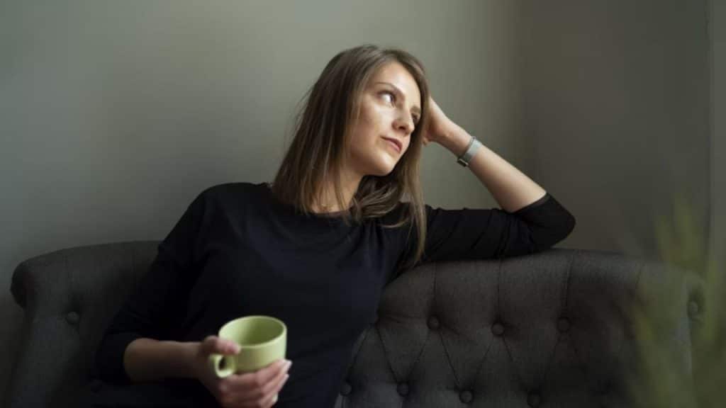 Woman sitting alone on the couch, staring thoughtfully into space