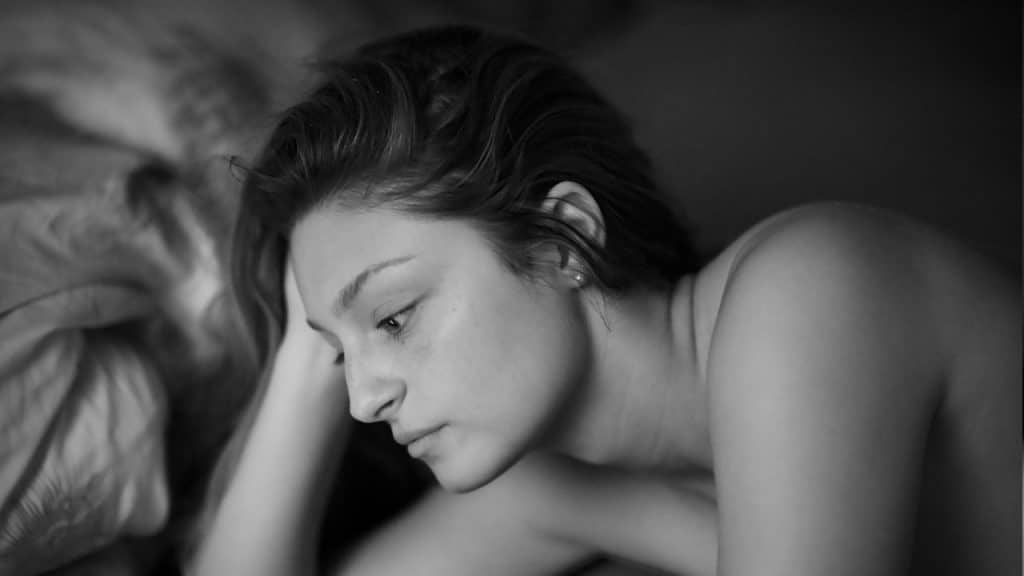 A close-up, black and white profile of a woman lying down, looking pensive or troubled, with her head resting on her hand.