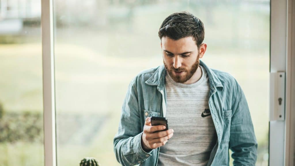 A person looking at his phone and leaning on a window.
