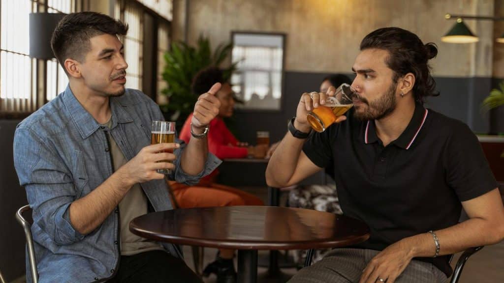 A pair of men sitting at a table drinking beer and talking.