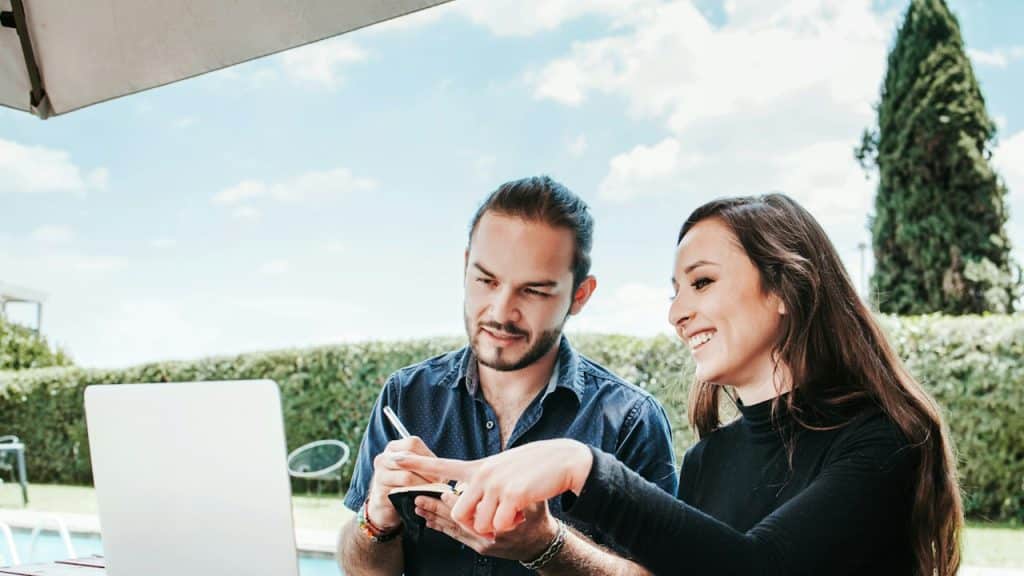 A man and a woman working on a laptop in the open air.