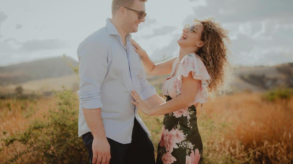 A couple laughing together outdoors in a sunny field.