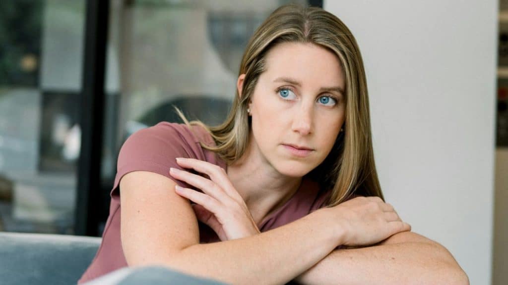 A young woman with blonde hair and blue eyes looks away seriously, resting her chin on her crossed arms.