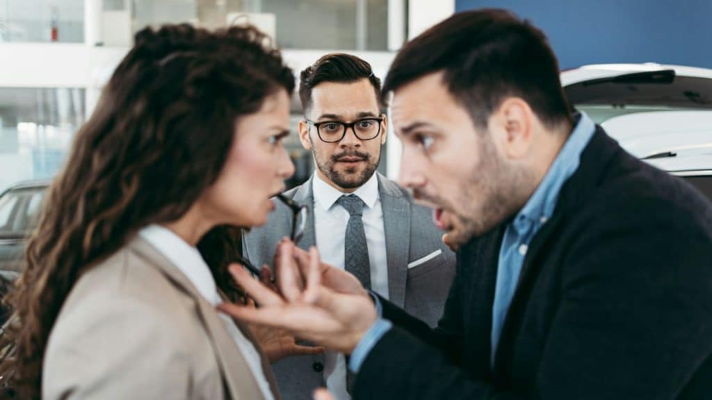 A heated argument between a woman and a man is interrupted by a second man in a suit with a shocked expression.