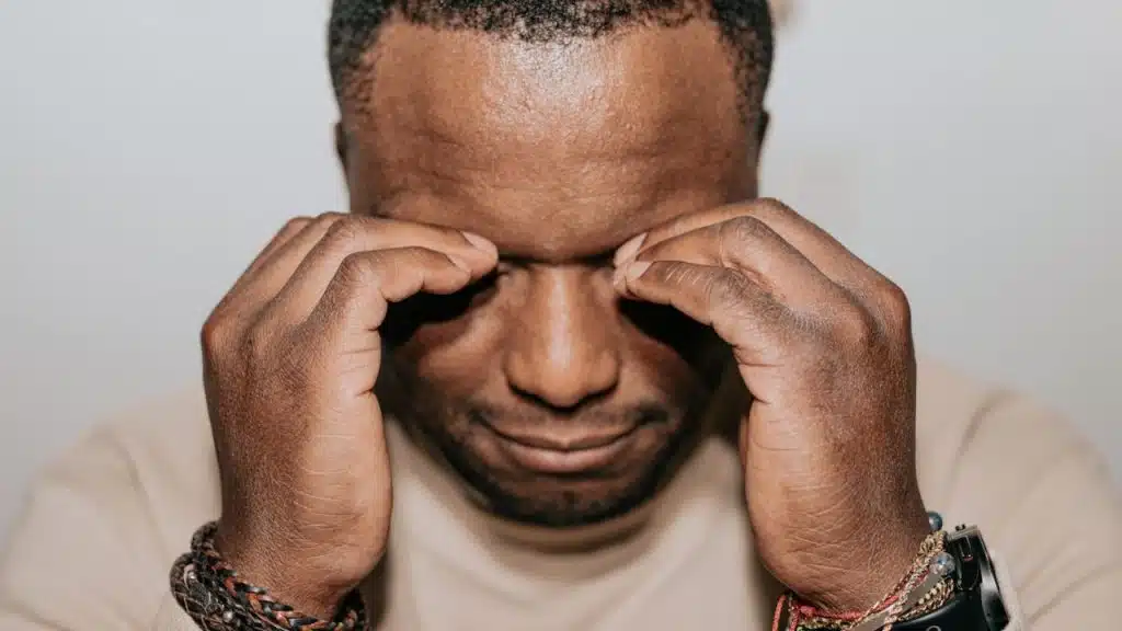 Close-up of a man with his eyes closed, rubbing his temples with both hands.