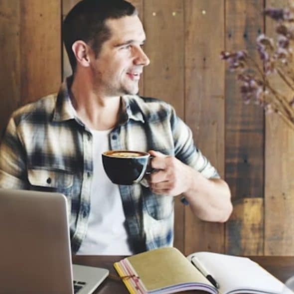 A thoughtful man sitting in a café, looking distant while holding a coffee mug