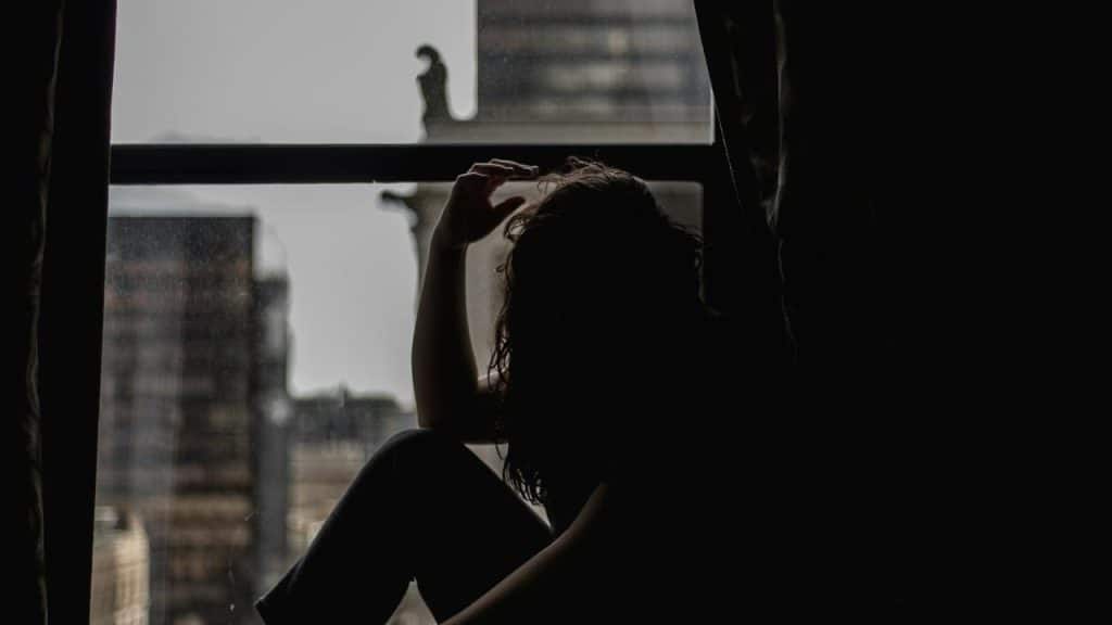 A person sitting by a window in shadow, looking outside.