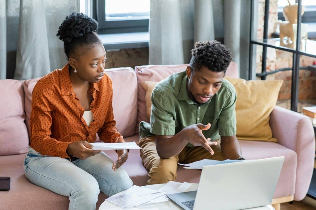 A serious African man sitting with wife and discussing finances.