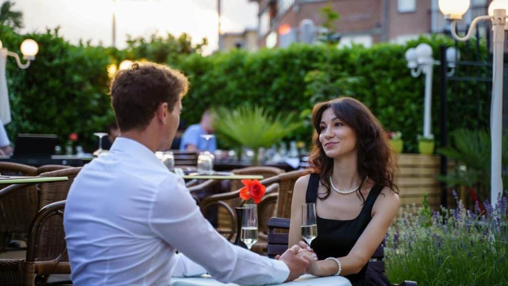 A couple holding hands and smiling at each other during an outdoor dinner.