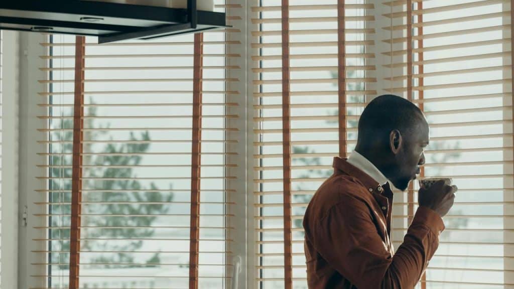 A man standing by a window drinking from a cup.